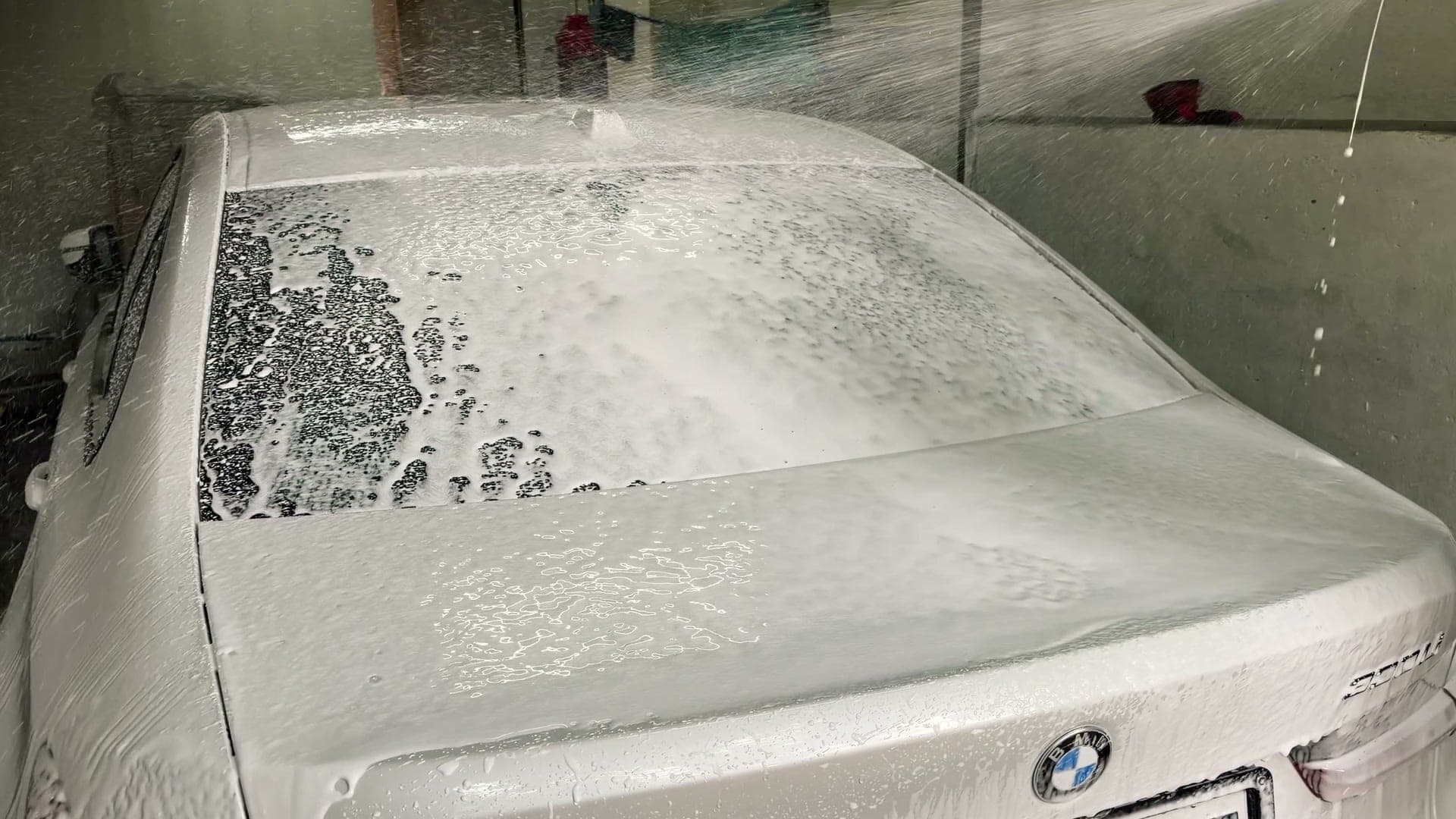 Snow foam covering a white BMW 330Li in the wash bay