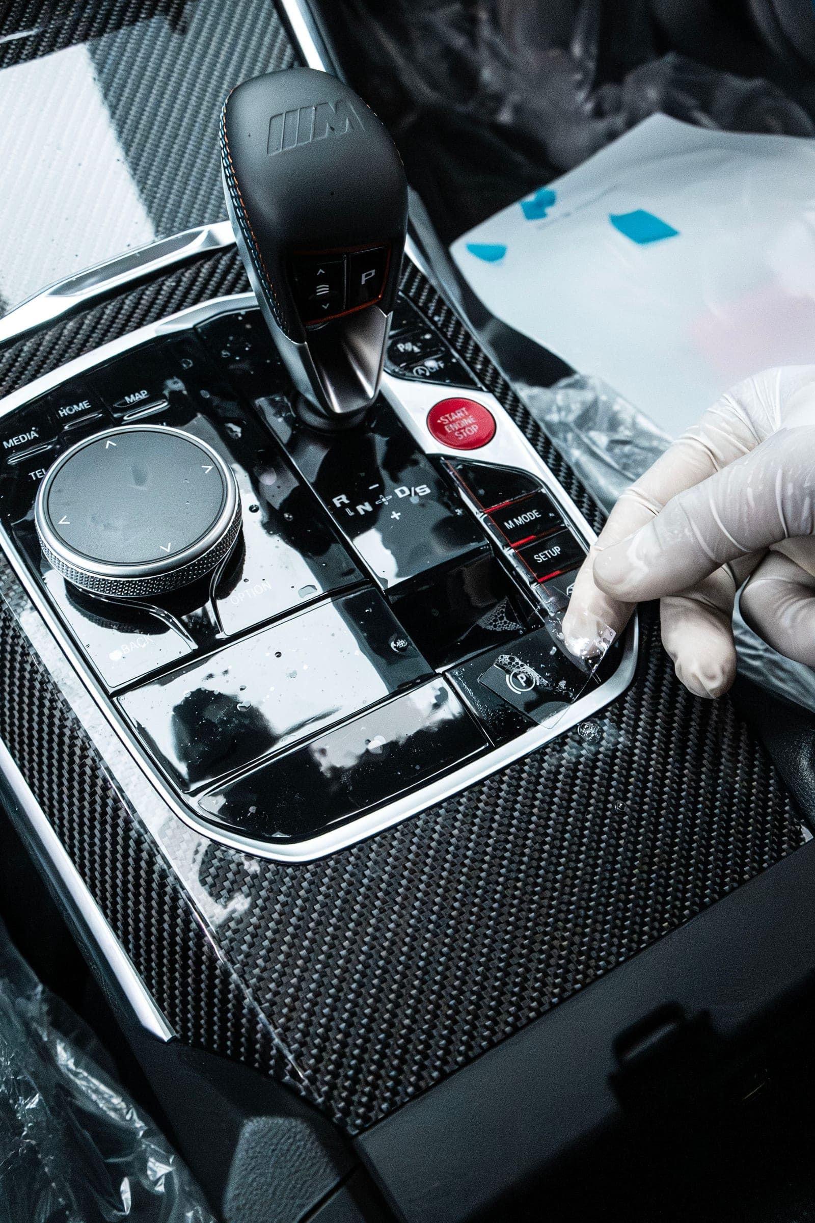 Gloved hand pressing film onto the gloss black gear-selector surround of a BMW M2