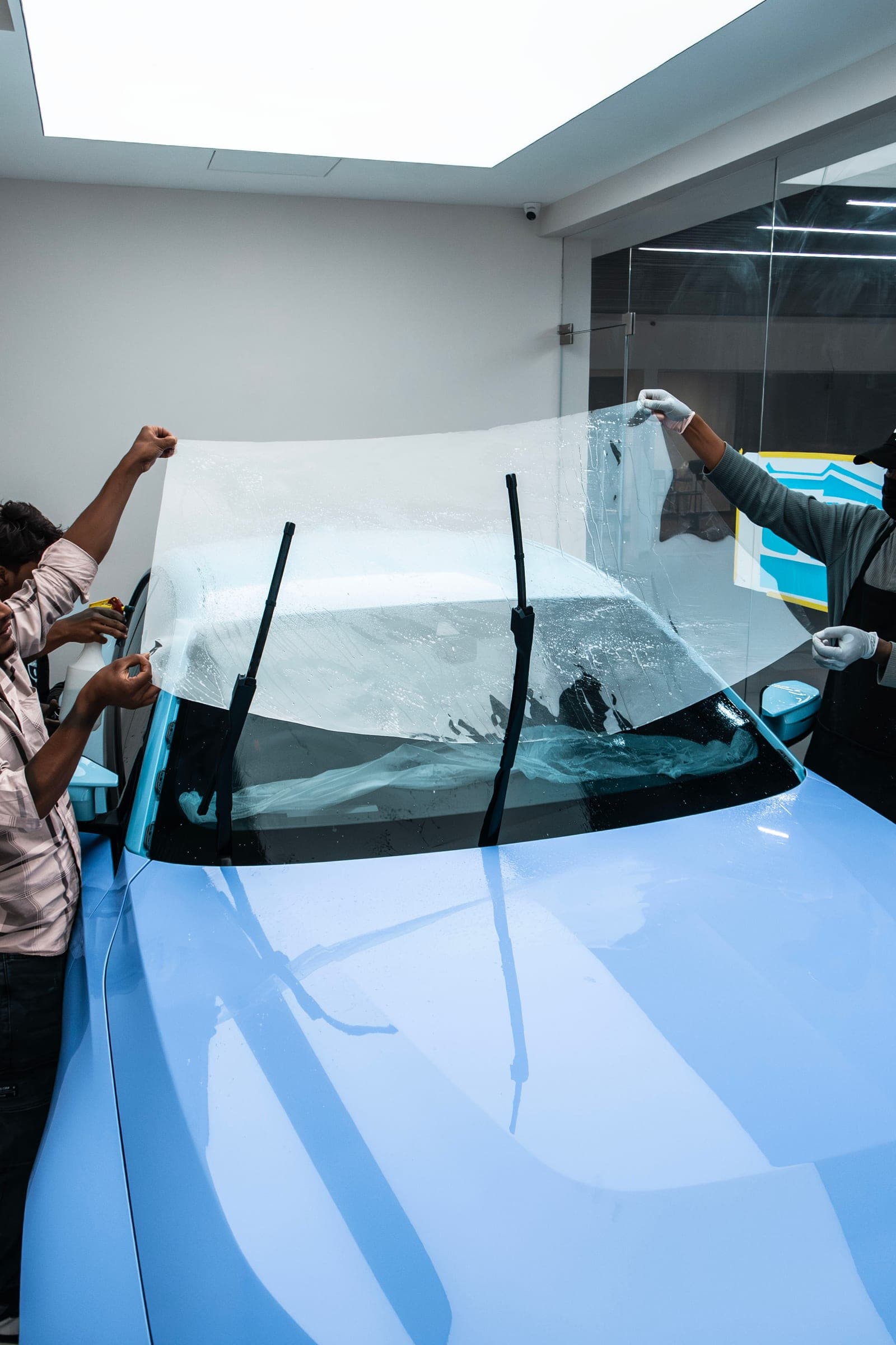 Two installers positioning a sheet of film over a BMW M2 windscreen