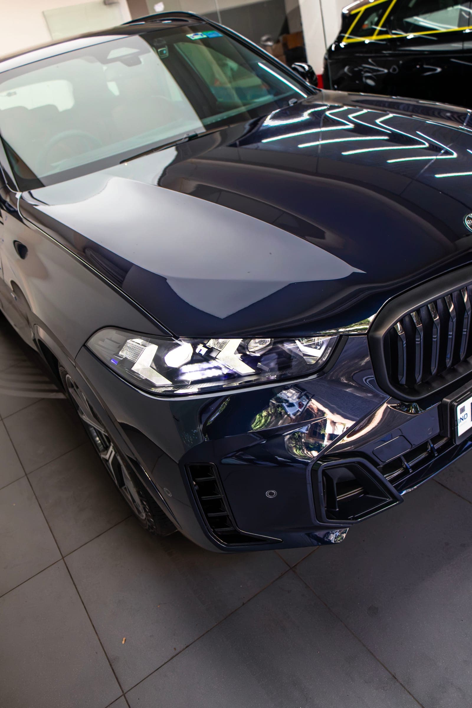 Studio light lines reflected across the bonnet and headlight of a dark blue BMW X5