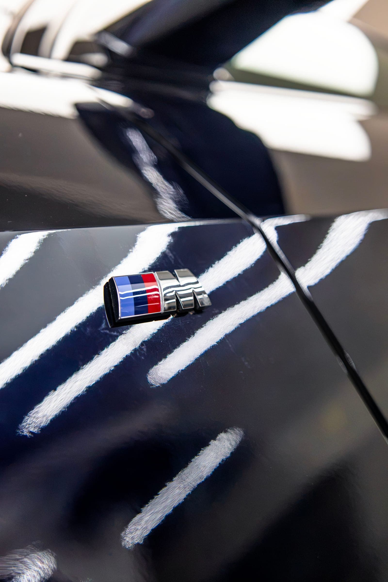 BMW M badge on a gloss wing, studio lights reflected in the paint