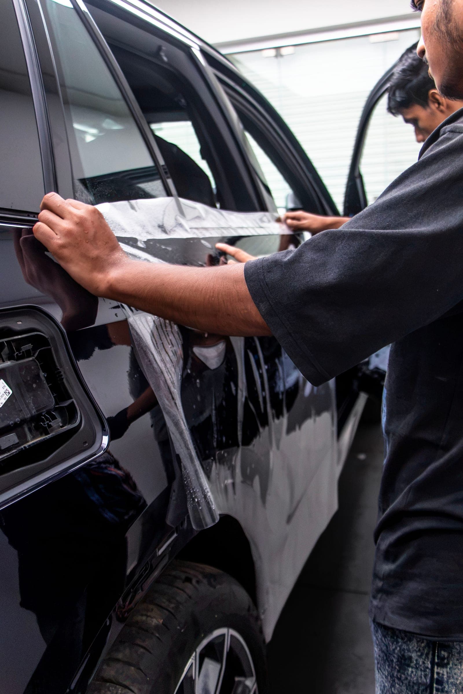 Installer positioning paint protection film on the door of a dark blue BMW X5