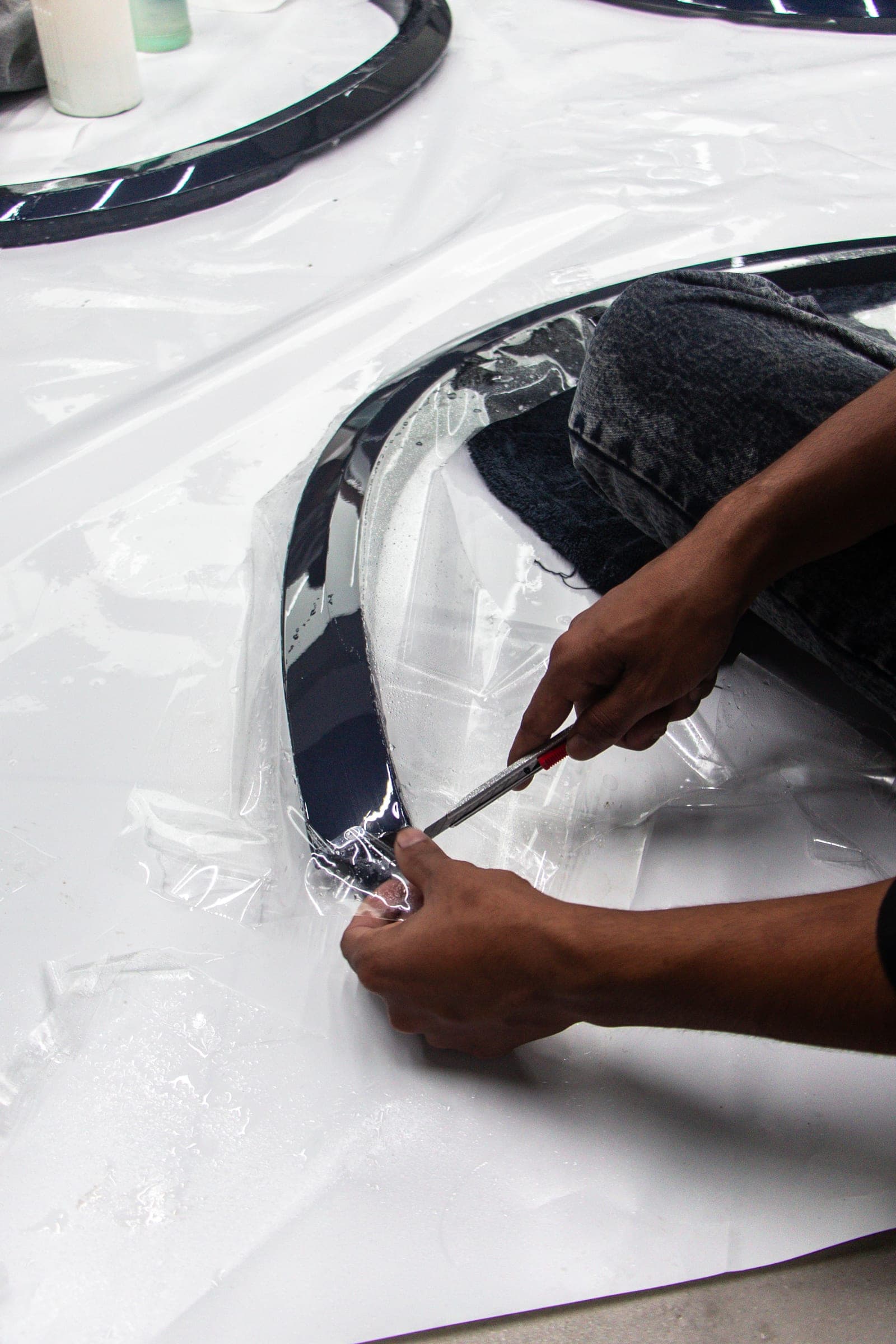 Paint protection film being trimmed around a removed trim component on the workbench