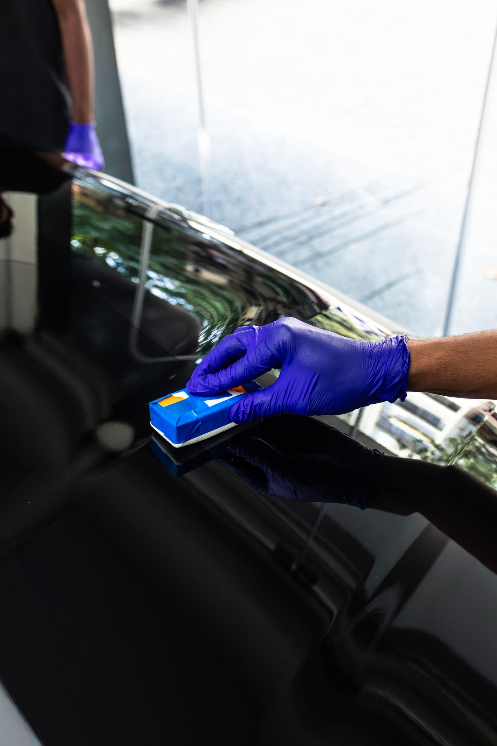 Violet-gloved hand working a ceramic coating applicator across black paint