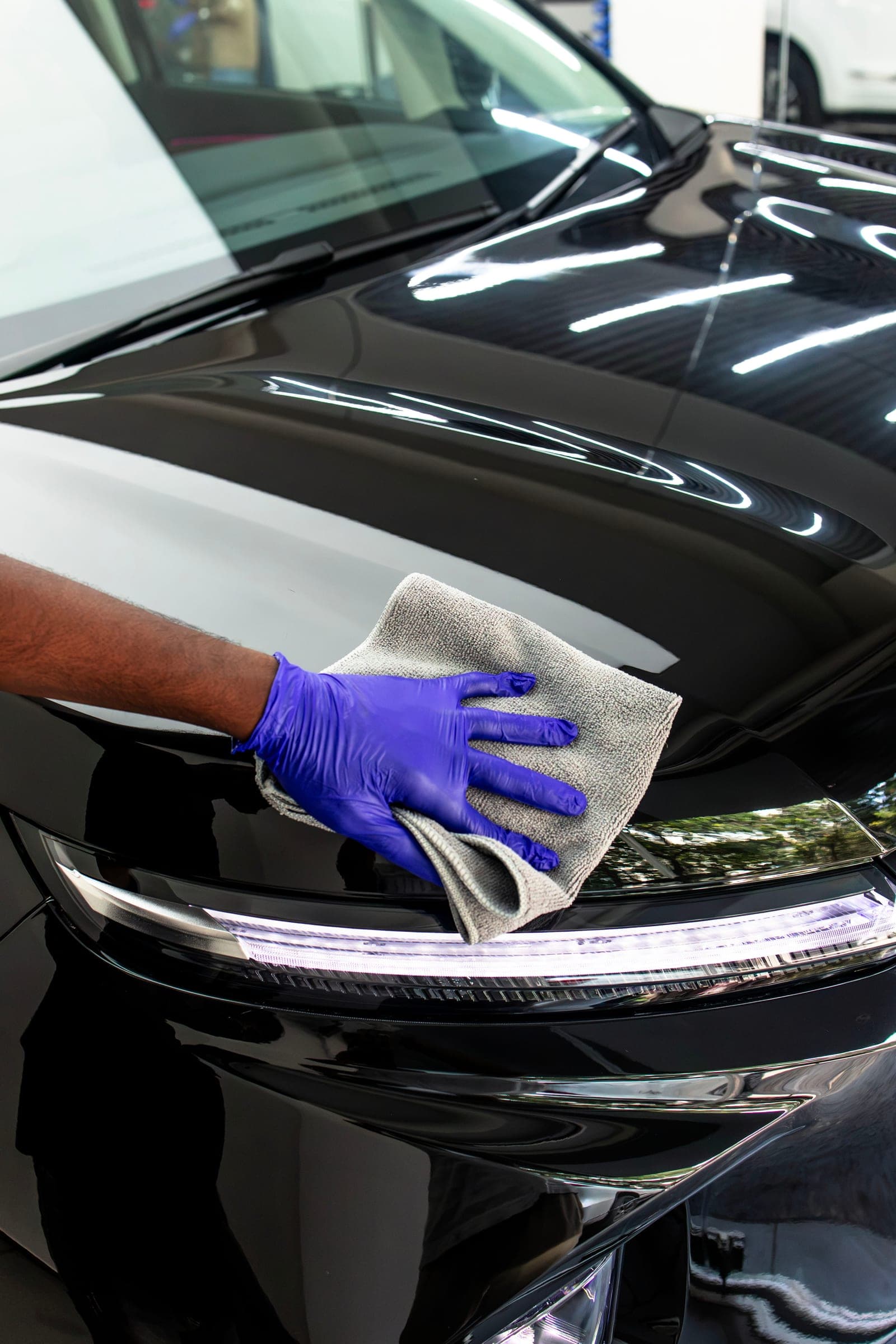 Technician levelling ceramic coating with a microfibre towel near the headlight
