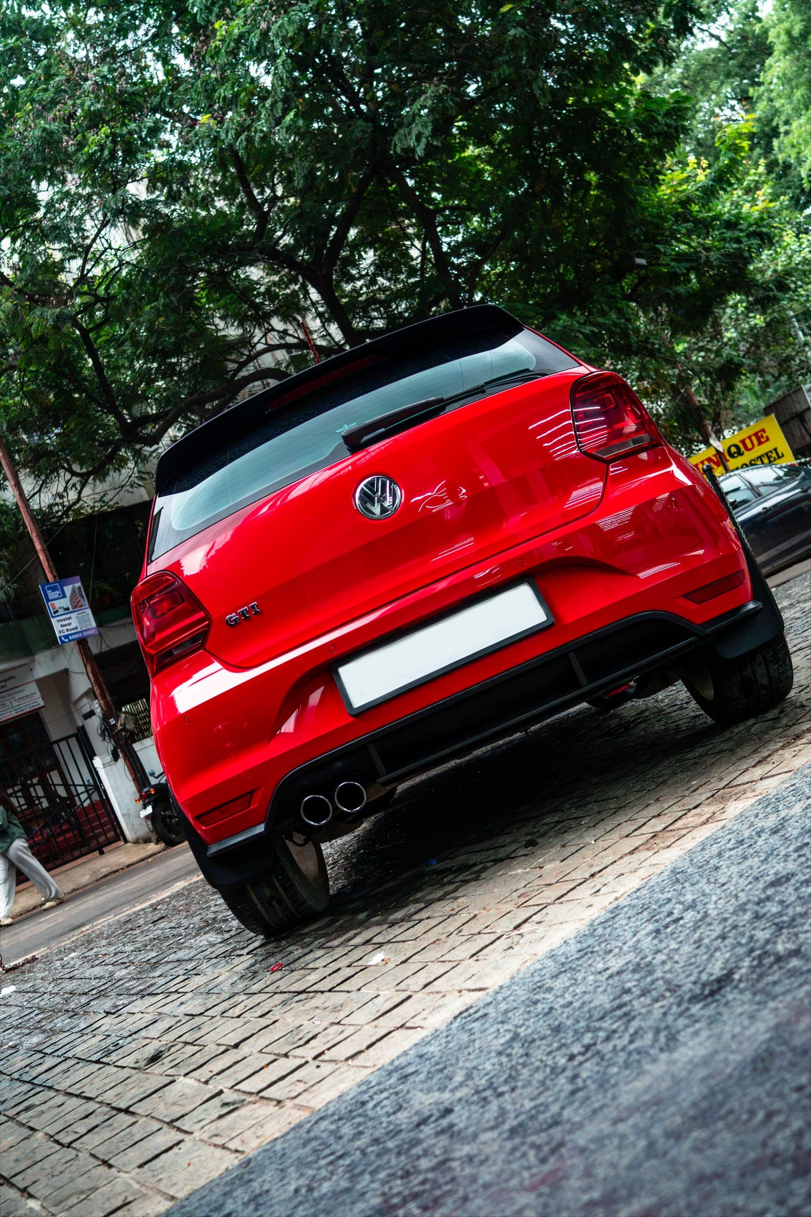 Rear three-quarter of a red Volkswagen Polo GT on a tree-lined Pune street