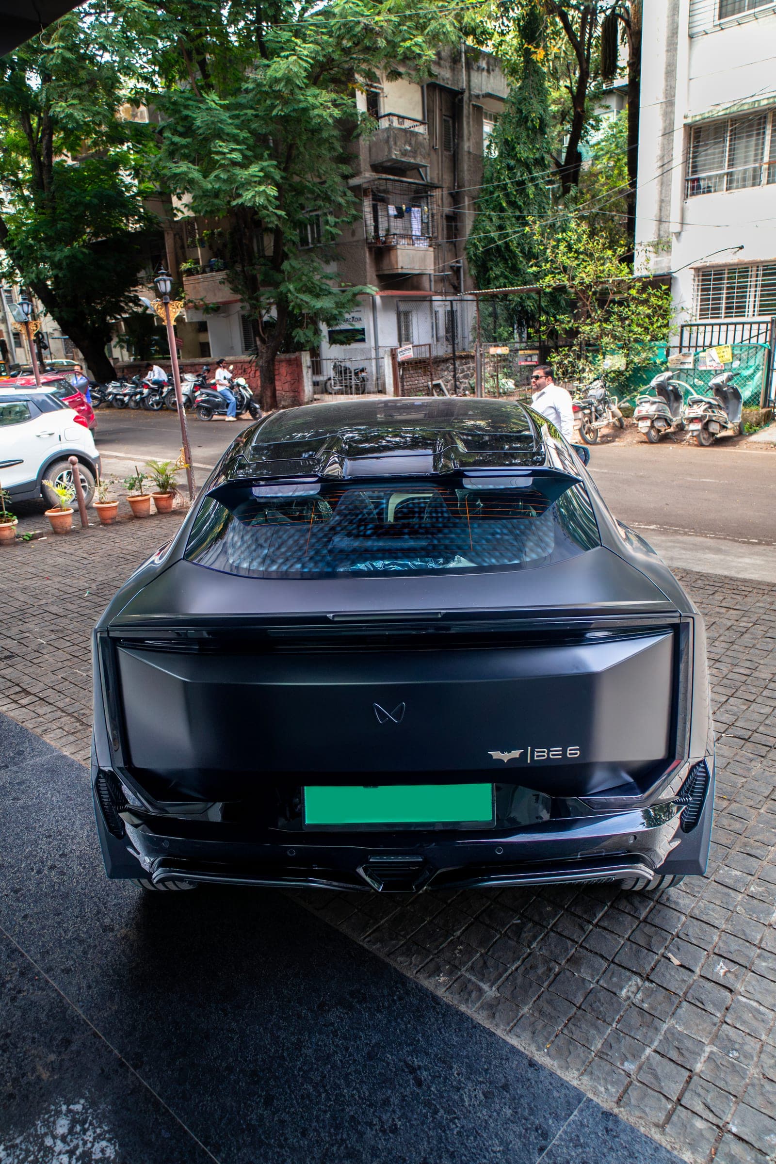 Rear of a satin black Mahindra BE 6 on a tree-lined Pune street