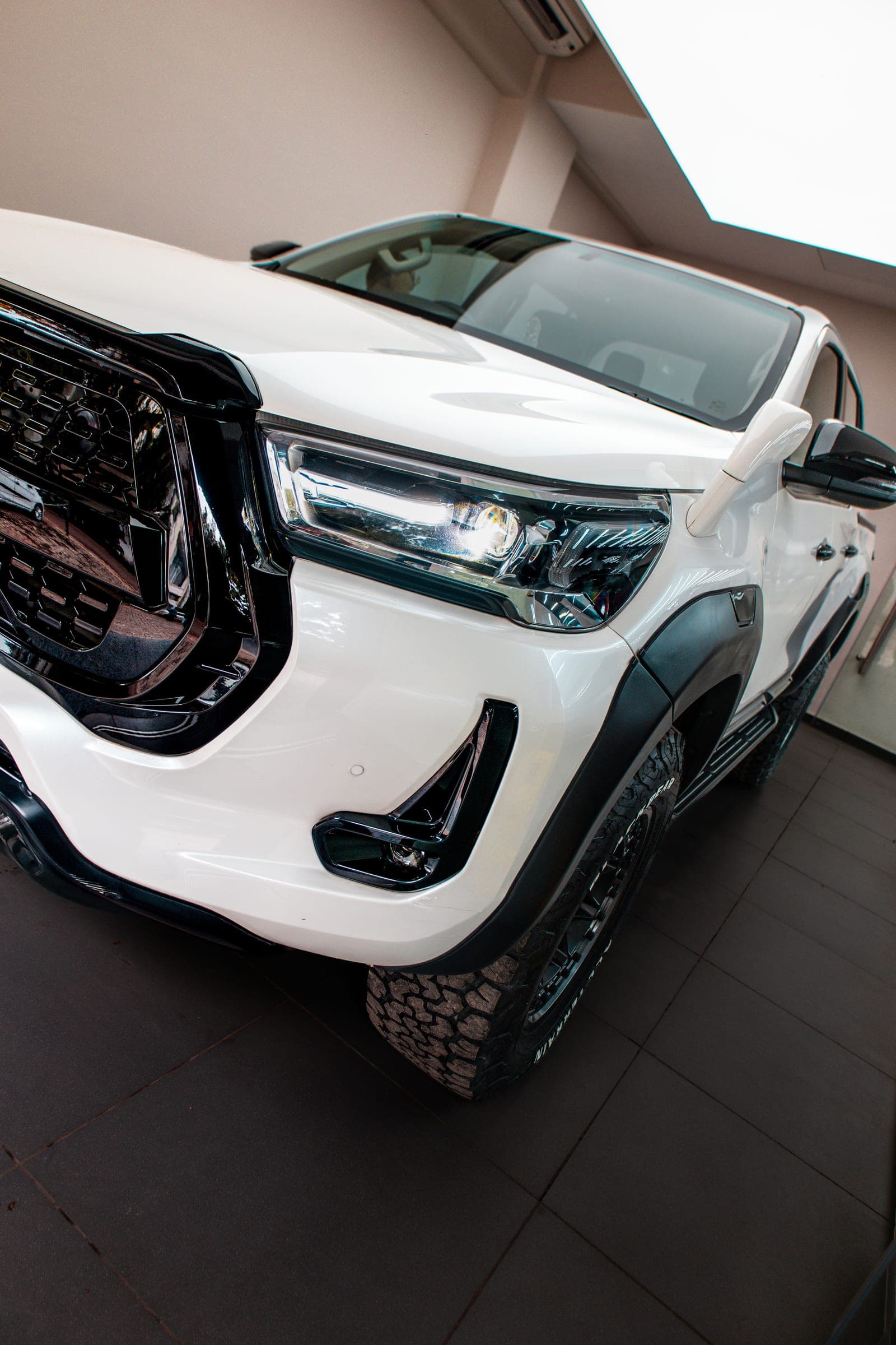 White Toyota Hilux on off-road tyres in the studio, low front three-quarter view