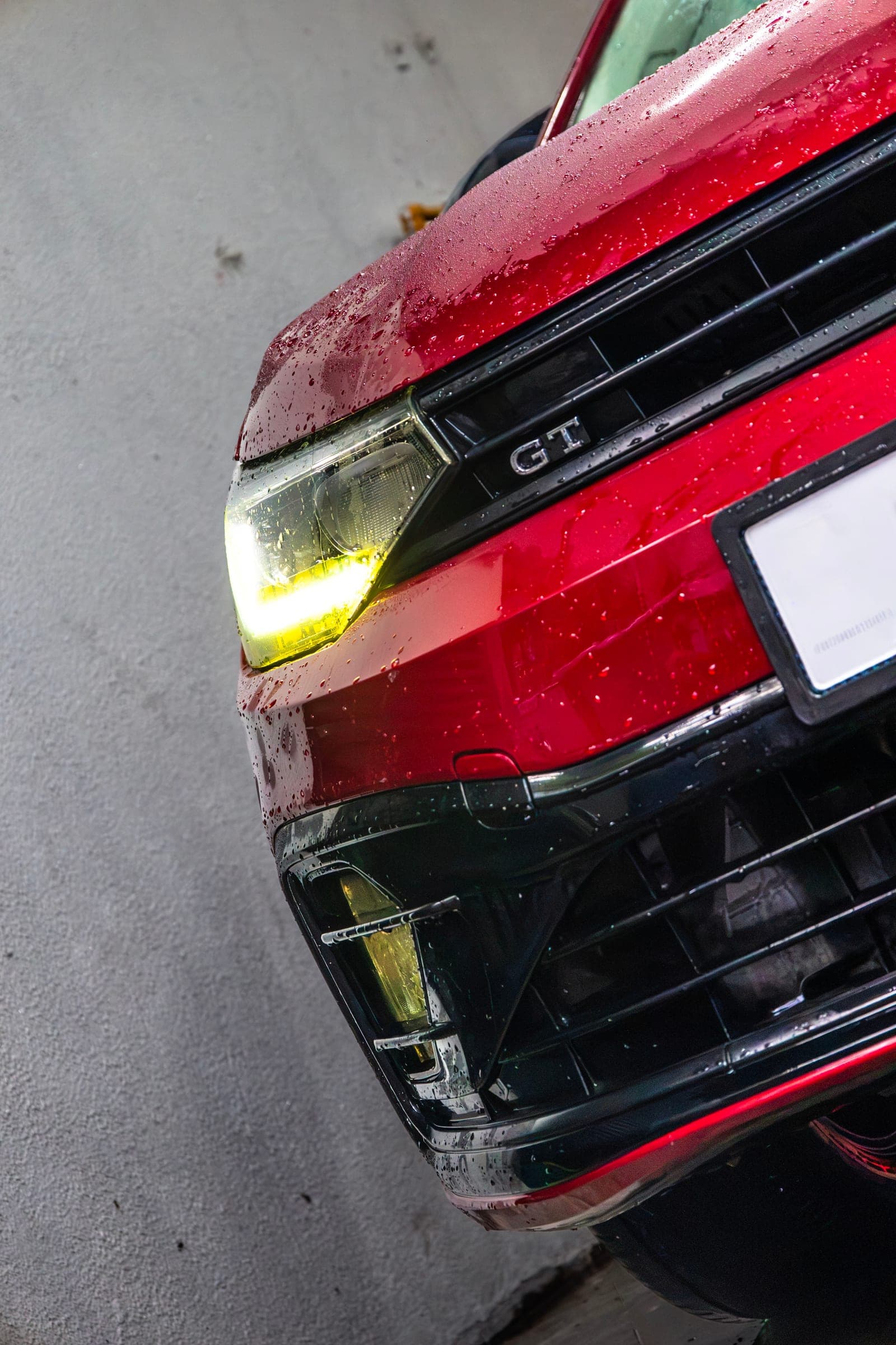 Water beading on the front corner of a red Volkswagen Virtus in the wash bay